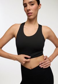 Top corto sportivo nero con scollatura rotonda e spalline larghe, realizzato in materiale liscio ed elastico, abbinato a leggings neri a vita alta.