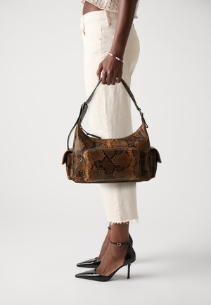 Sac à main en cuir synthétique imprimé serpent brun et noir avec une silhouette courbée, deux poches latérales et une bandoulière ajustable. Assorti avec un pantalon blanc cropped et des talons noirs.