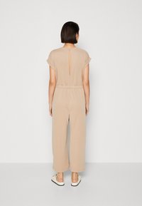 Beige jumpsuit met korte mouwen, elastische taille en een sleutelgatdetail aan de achterkant. Vloeiende, lichtgewicht stof met wijde pijpen.