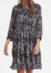 Mörkblå blommig klänning med långa ärmar, med en avslappnad passform, lager-på-lager-design och vita och beige blommönster på ett genomskinligt material.