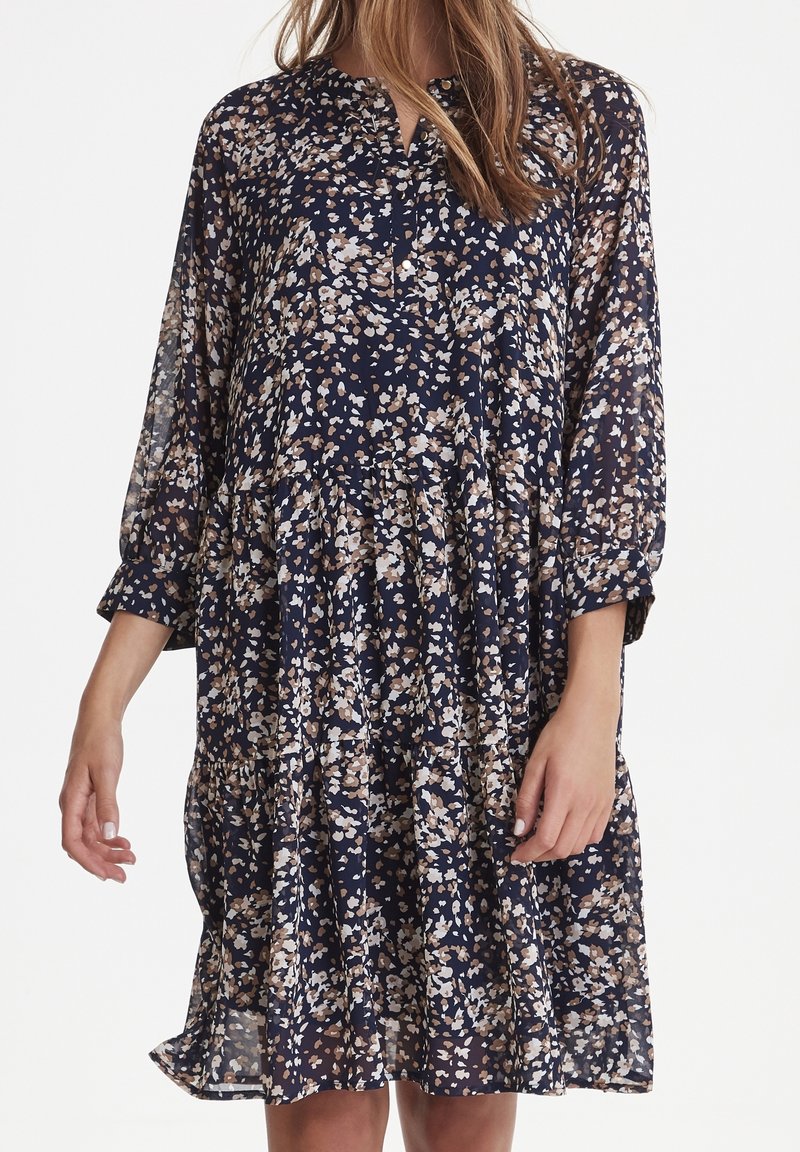 Mörkblå blommig klänning med långa ärmar, med en avslappnad passform, lager-på-lager-design och vita och beige blommönster på ett genomskinligt material.