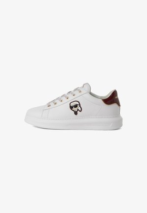 Vita lädersneakers med gyllene öglor, grå snören, vinröd hälaccent och en svart och vit serietidningslogotyp på sidan.