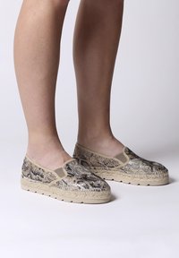 Instap schoenen met een gestructureerd slangenprintontwerp in beige en zwart, met een natuurlijke geweven zool en elastische zijpanelen voor comfort.