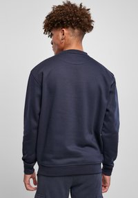 Sudadera azul marino con cuello redondo, puños y dobladillo acanalados, hecha de una tela suave, llevada por una persona vista desde atrás.