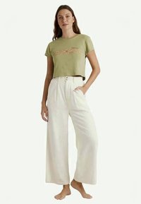 T-shirt court vert olive avec broderies florales, associé à un pantalon blanc large avec deux boutons et un tissu texturé.