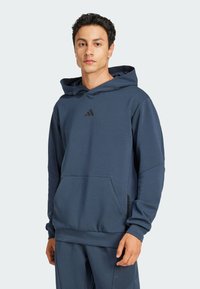 Dunkelblauer Kapuzenpullover aus weichem Stoff, mit einer Kängurutasche, gerippten Bündchen und einem schwarzen Logo auf der Brust.