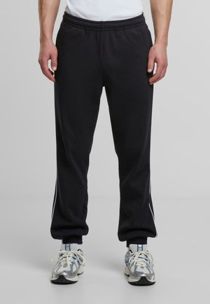 Schwarze Sporthosen aus glattem Stoff. Mit einem elastischen Bund und weißen Streifen an den Seiten. Schmal zulaufende Bündchen an den Knöcheln.