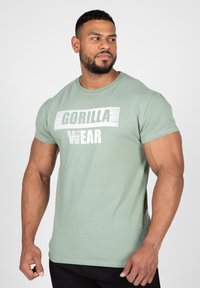 Groene katoenen t-shirt met een witte grafiek waarop "GORILLA WEAR" in vette letters staat. Korte mouwen en een ronde hals ontwerp.