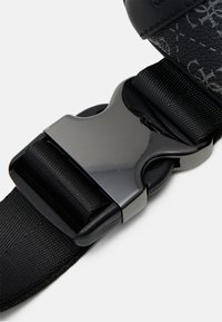 Black fabric strap with a glossy black plastic buckle. Features a textured strap and a smooth, shiny buckle. Close-up view emphasizing details.