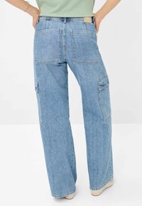 Hellblaue Cargo-Jeans mit weiten Beinen, ausgestattet mit zwei hinteren Taschen und einer seitlichen Utility-Tasche. Hergestellt aus Denim mit einem gewaschenen Finish.