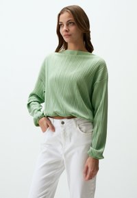 Maglione a coste verde chiaro con maniche lunghe, scollatura ampia e tessuto testurizzato, abbinato a jeans bianchi a vita alta.