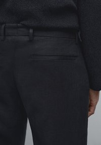Black linen trousers featuring a smooth texture, a flat back pocket, and a slim silhouette, paired with a dark knit sweater.