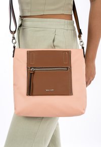 Bolso de hombro con un material exterior suave de color rosa, que presenta un bolsillo frontal de cuero texturizado marrón con un zipper plateado y costuras de acento.