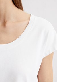 Vit t-shirt med en bred, rund halsringning och korta ärmar. Tyget har en slät textur och en klassisk snitt.