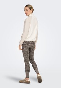 Veste en polaire taupe clair avec col montant ; associée à des leggings sombres à motifs et des baskets marron avec des bandes blanches.