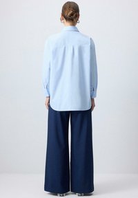 Camicia azzurra chiara a maniche lunghe con colletto a punta, orlo curvo e polsini con bottoni, abbinata a pantaloni larghi blu navy.