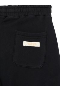 Sorte sweatpants med elastisk talje, baglomme med syede kanter og et mærke med orange tekst på hvid baggrund.