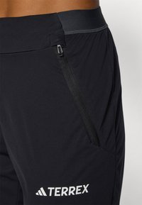 Pantalons de plein air noirs avec une texture lisse, une taille élastique, une poche zippée et le logo "TERREX" en blanc sur la jambe.