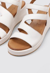 Sandalias de cuña blancas con múltiples correas cruzadas, parte superior de cuero suave, plantilla texturizada marrón y suela gruesa de goma blanca.