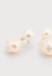 Boucles d'oreilles en perles avec monture en or ; comprenant deux tailles de perles blanches lisses, la plus grande ayant un petit trou et étant fixée à un clou.