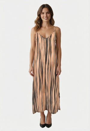 Joven sonriente, vestida con un vestido midi sin mangas con rayas verticales en color durazno y negro, y tacones negros, posando frente a un fondo blanco.