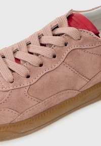Sneaker in suede rosa chiaro con lacci in tessuto, tomaia testurizzata e suola in gomma. Presenta un tallone in pelle rossa e dettagli di cucitura discreti.