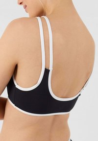 Top sportivo nero con bordini bianchi, caratterizzato da un design racerback e spalline sottili. Il materiale sembra liscio ed elastico con pochissimi accessori.