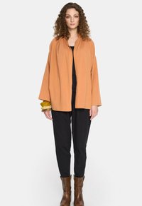 Lekki, pomarańczowy żakiet w stylu kimona o luźnym kroju, zestawiony z czarnymi spodniami i brązowymi botkami za kostkę. Uzupełniony bransoletką.