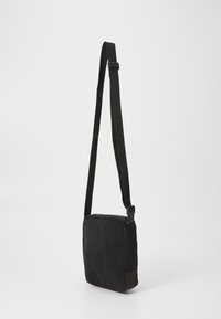 Bolso cruzado negro con un tejido texturizado, correa tejida ajustable, cierre con cremallera y un panel inferior sólido.