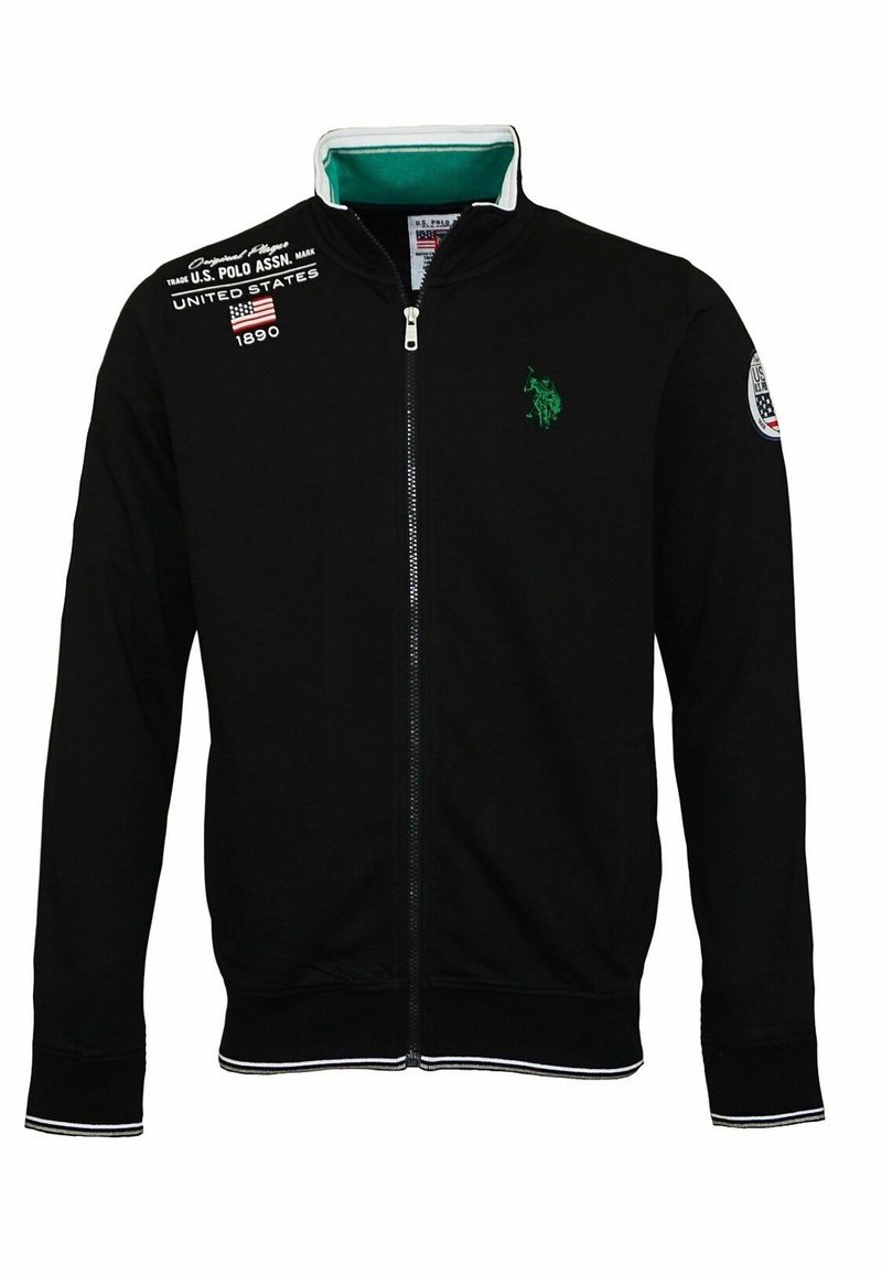 Black zip-up jacket made of cotton. Features a green logo, white accents on cuffs and collar, and patches on the left shoulder.