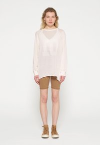 Maglione a maniche lunghe leggero e arioso di colore bianco sporco, abbinato a pantaloni ciclisti aderenti color sabbia e sneakers alte marroni. Silhouette rilassata, maniche raglan.