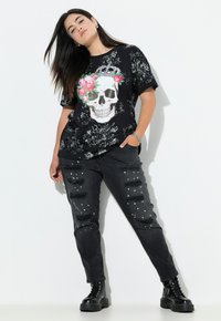 Zwarte t-shirt met een schedel en bloemenaccenten, gecombineerd met versleten zwarte spijkerbroeken met witte parel-details en zwarte combat boots.
