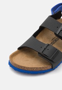 Sandali neri con due cinturini regolabili, materiale testurizzato, soletta in sughero e suola in gomma blu. Presentano dettagli in metallo brandizzati.