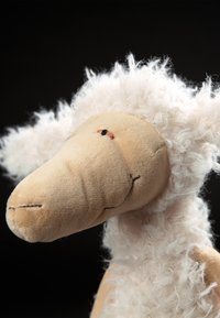 Stuffed animal sheep with a soft, fuzzy white body, beige face, and stitched mouth and eyes, featuring a rounded snout and curly wool accents.