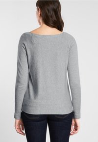 Gray long-sleeve sweater with a wide neckline, made from a soft fabric, features a slightly fitted silhouette and is paired with dark jeans.