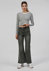 Flared gray denim jeans with a high waist, front-button closure, and two side pockets, paired with a black-and-white striped long-sleeve top.
