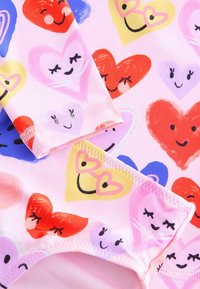 Bañador con corazones multicolores en varias tonalidades sobre un fondo rosa. El material es suave con un ajuste flexible y costuras decorativas.