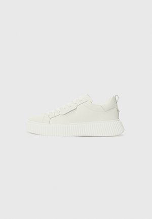 Witte lage sneakers met dikke ribbelzool, vetersluiting aan de voorkant en een instaplus aan de hiel op een effen lichte achtergrond.
