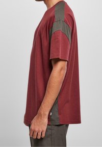 Camiseta de manga corta color granate con detalles en gris en los hombros. Confeccionada en tela suave, presenta un ajuste relajado y detalles de costuras en los laterales.