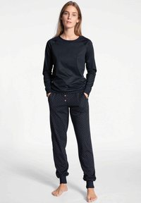 Long-sleeve black top paired with dark blue polka dot pajama pants featuring cuffed hems and three-buttons at the waistline.