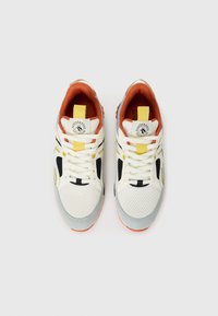 Sneakers with a mesh upper in off-white, grey accents, and orange heel. Features black and yellow details, textured laces, and logo patch.