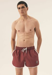 Męskie szorty kąpielowe w kolorze bordowym z elastycznym pasem, białym sznurkiem do regulacji, bocznymi kieszeniami i kontrastowymi białymi wykończeniami. Zawierają detal logo po boku.