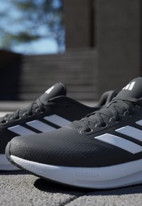 Black athletic shoes with white stripes, mesh texture, and Cloudfoam branding. Features a rounded toe and flat sole.