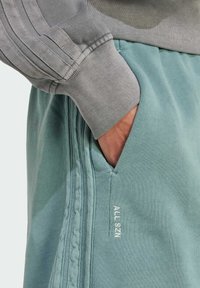 Lys grå sweatshirt med ribbede manchetter, parret med teal sweatpants med sidelommer og "ALL SZN" broderet i hvid.