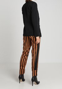 Czarna, dopasowana marynarka w komplecie z wysokimi, paskowanymi spodniami w kolorze pomarańczowym i czarnym. Spodnie mają taperedowy kształt i mankiety przy kostkach.