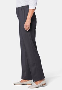 Pantalons larges gris foncé en tissu texturé, avec une taille élastique, coupe droite, associés à des chaussures plates de couleur claire.