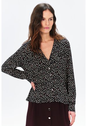Blusa negra de botones con patrones de corazones blancos y rojos. Presenta un cuello en V y mangas largas. Tejido suave con un corte holgado.