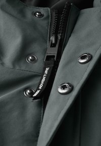 Green waterproof jacket with black zipper, silver snaps, and textured fabric. Features label reading "ADVENTURE" attached to the zipper.