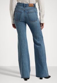 Høytlivede blå denim flared jeans med en teksturert overflate. Har to baklommer og et lærmerke på midjebåndet.