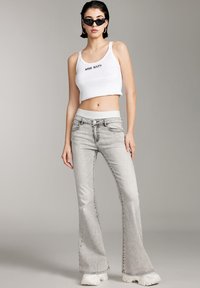 White fitted crop top with "MISS SIXTY" logo, paired with light grey flared jeans. Textured denim, wide legs, and chunky white sneakers.